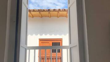Habitación con ventana que da a un edificio con tejado de tejas y puertas anaranjadas.