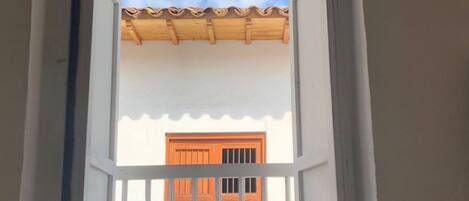 Quarto com janela que dá para um edifício com telhado ladrilhado e portas laranja.
