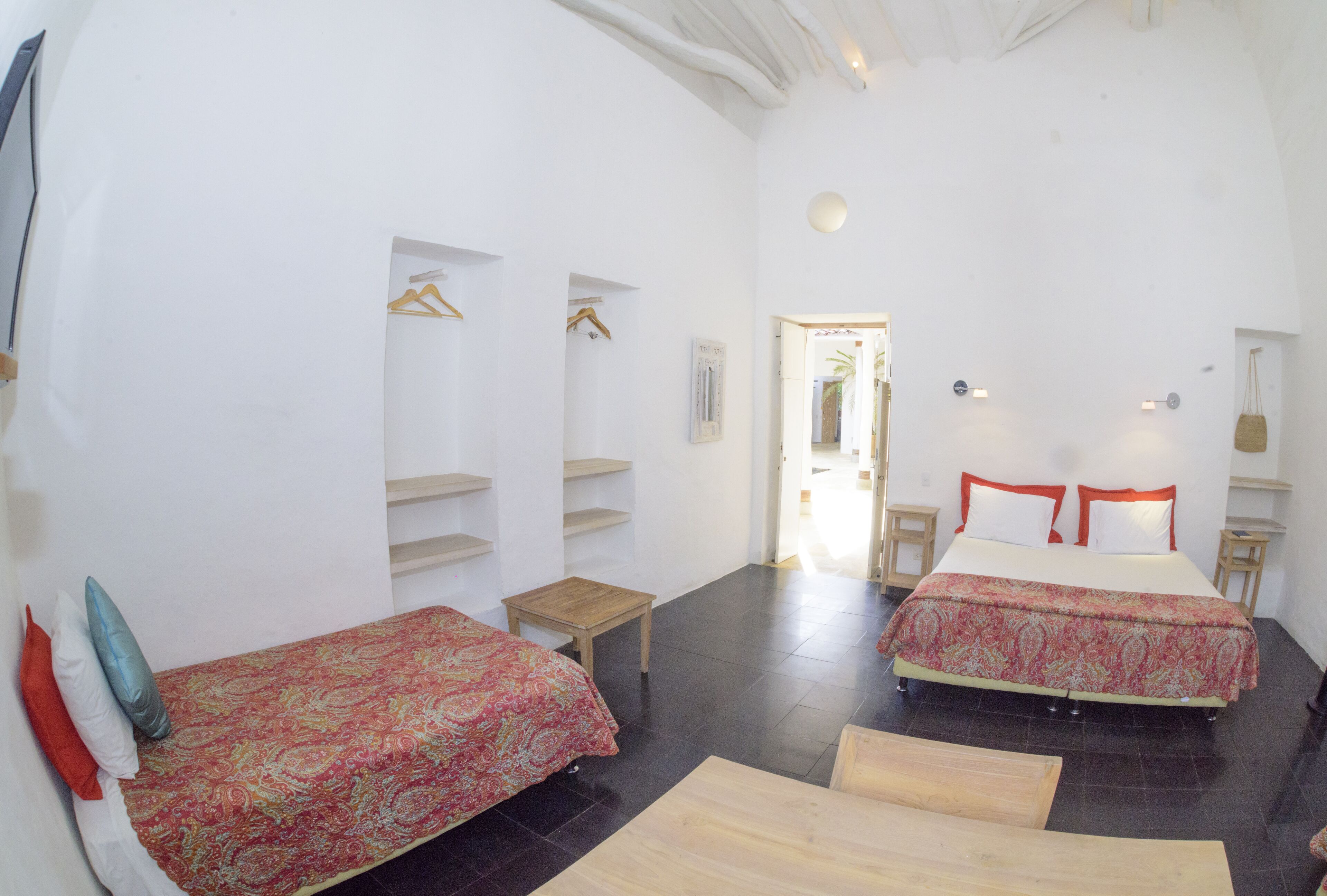 Quarto com duas camas, uma mesinha e uma porta que dá para outro espaço.