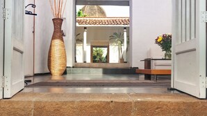 Entrada de hotel con un gran jarrón de mimbre, un banco y vistas del interior a través de una puerta de cristal.