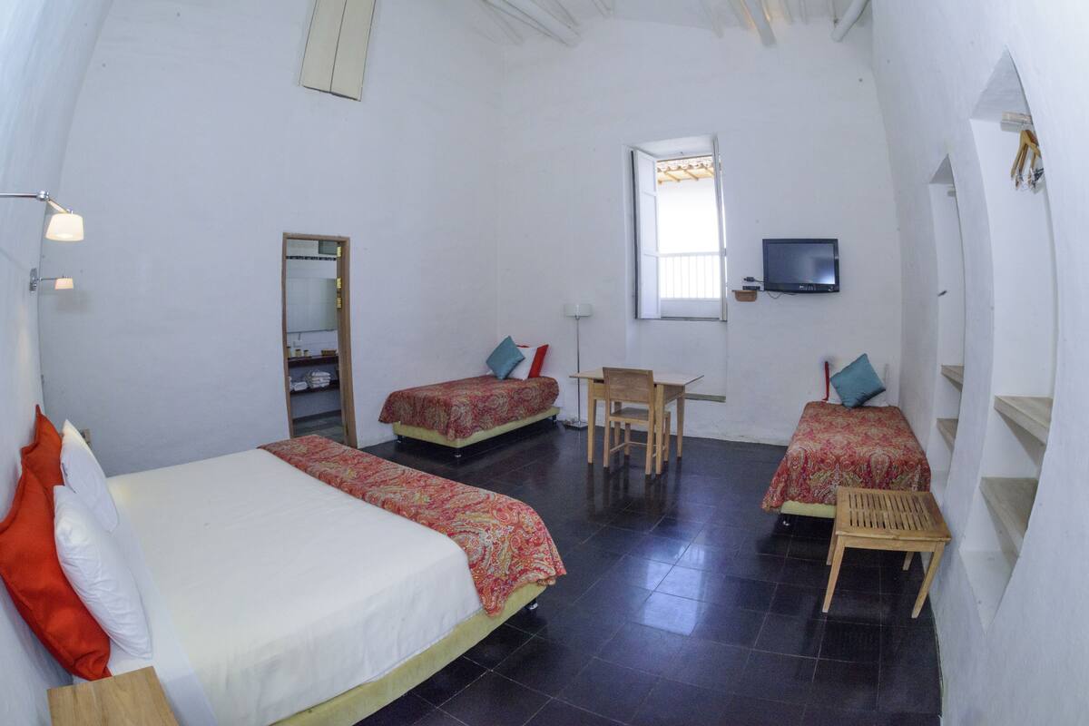 A room with two beds, a desk, a chair, a TV, and a window.