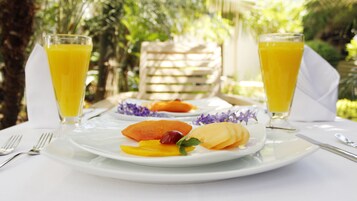 A breakfast setting with a plate of fruit, two glasses of orange juice, and a white tablecloth.