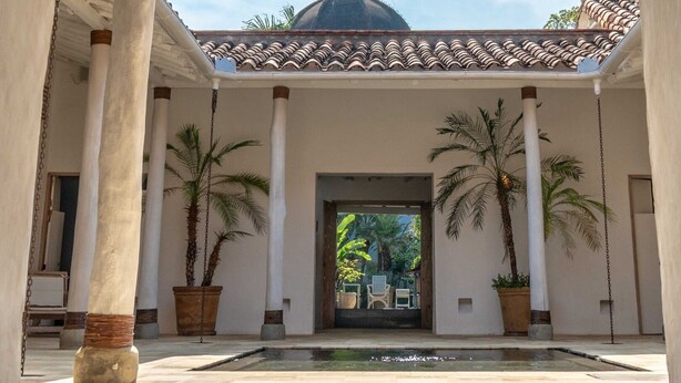 Un patio con una fuente, palmeras y un edificio con cúpula al fondo.