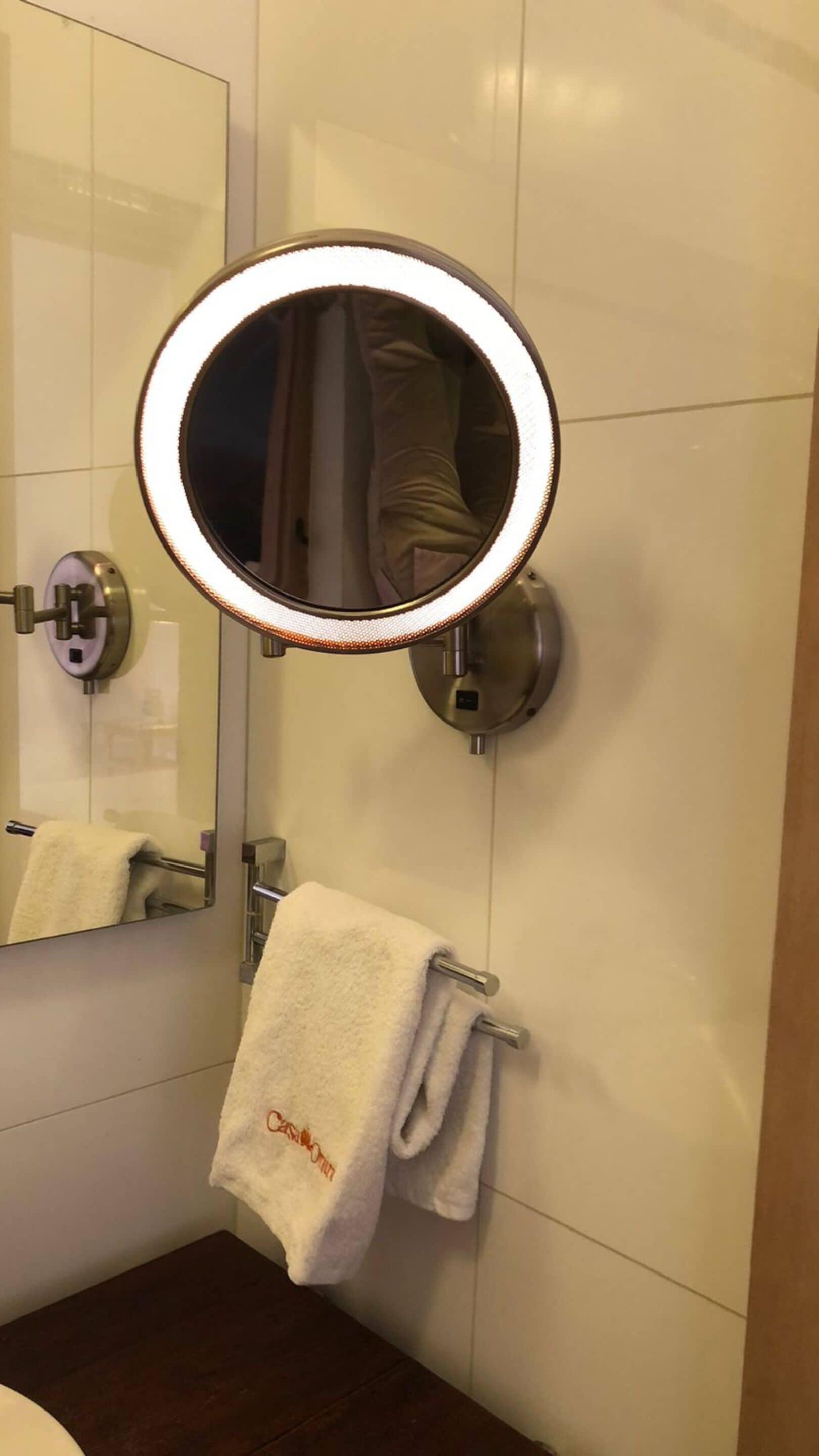 Et badeværelse med et spejl på væggen, en bøjle med et hvidt håndklæde og et toilet.