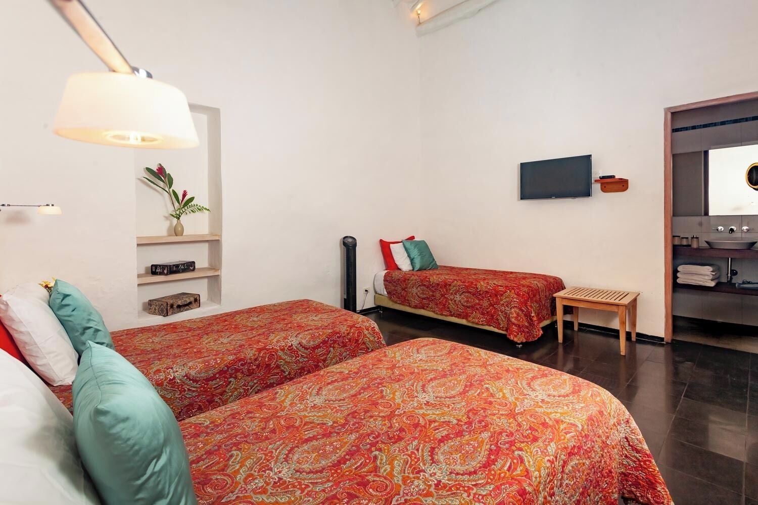 A modern hotel room with two beds, a TV, a small table, and a bathroom visible through an open door.