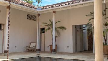 Un espacio al aire libre techado con piscina, palmeras y una silla.