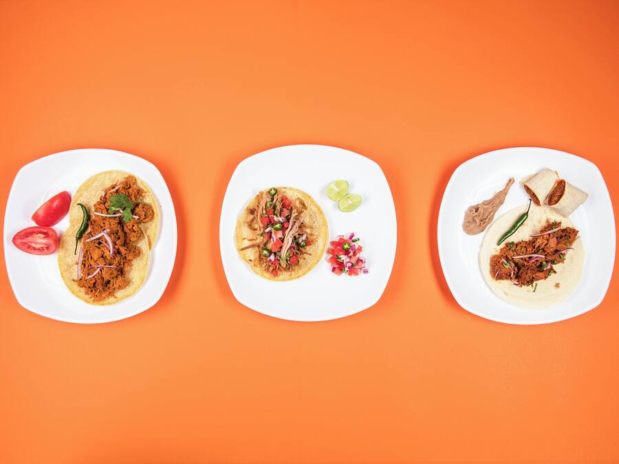 Three white plates with different food items on an orange background.