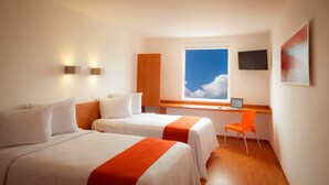 Une chambre d’hôtel avec deux lits, un bureau avec un ordinateur portable, une télévision et une fenêtre donnant sur le ciel.