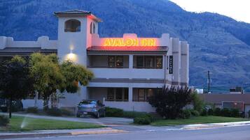 Exterior del Avalon Inn con un llamativo letrero de neón, un telón de fondo de montañas y un coche estacionado al frente.