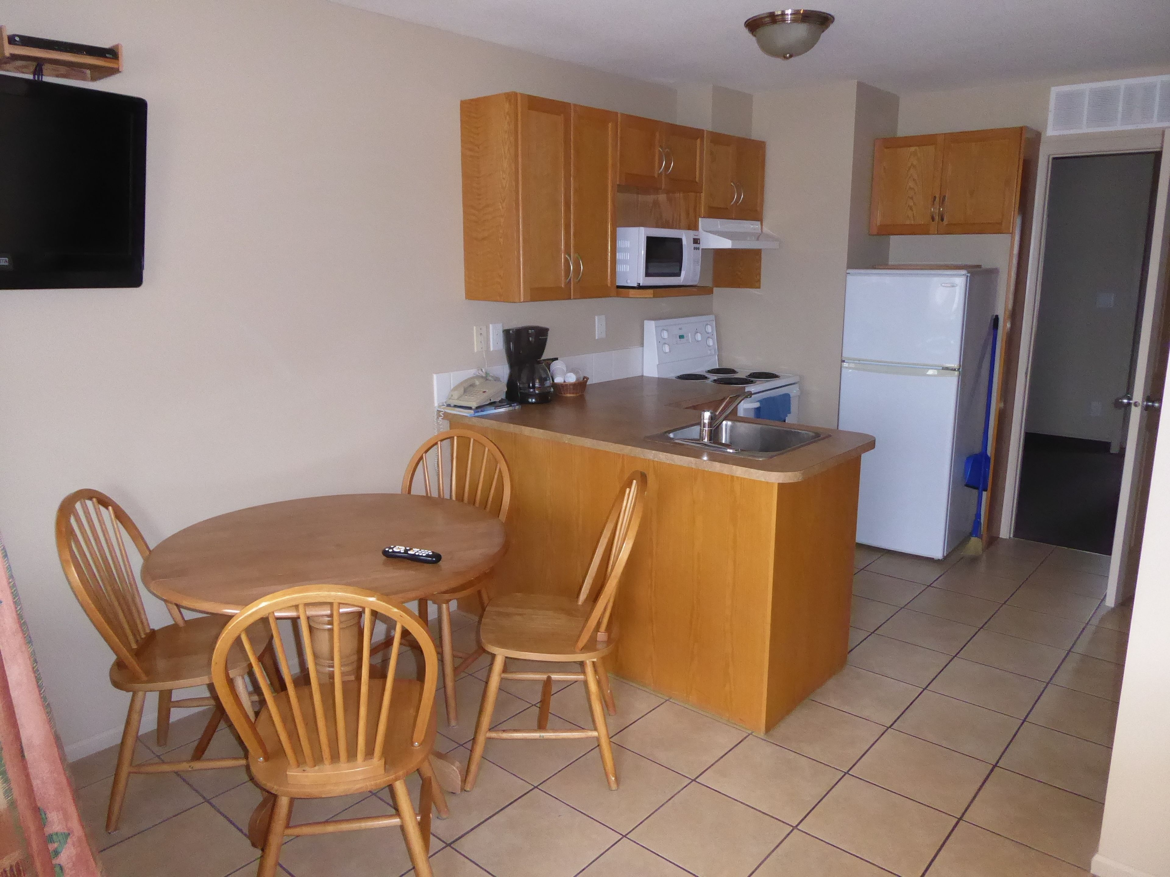 A compact kitchen with wooden cabinets, a microwave, a stove, and a refrigerator. There is a small dining area with a table and chairs.