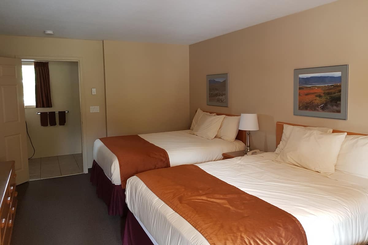 A hotel room with two beds, a bathroom, and a window with curtains.