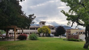 A hotel with a garden area, outdoor seating, and a view of mountains in the background. - Avalon Inn (Osoyoos)