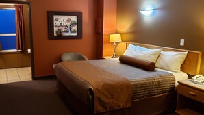 A hotel room with a bed, a bedside lamp, a telephone, a chair, and a painting on the wall. - Avalon Inn (Osoyoos)
