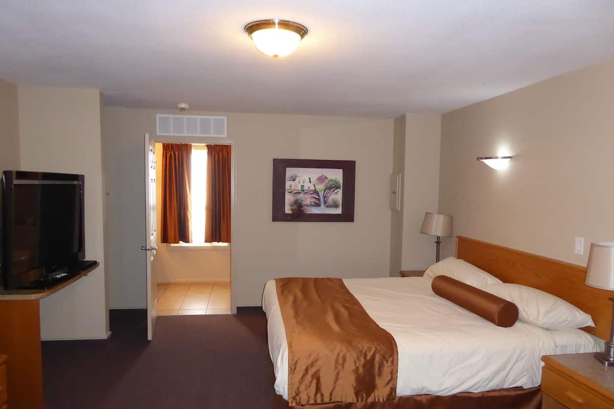 A hotel room with a bed, a TV, a painting, a lamp, and a door leading to another room.