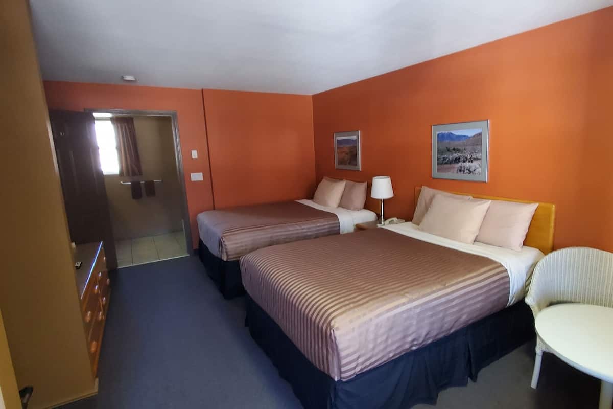 A hotel room with two beds, a chair, a small table, and two framed pictures on the wall.