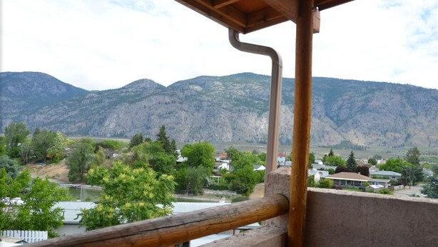 A balcony with a view of a mountainous landscape and a small town below. - Avalon Inn (Osoyoos)