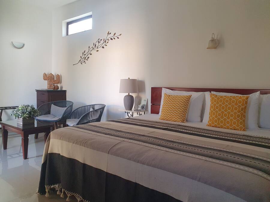 Une chambre d’hôtel avec un grand lit, un bureau avec une lampe, une chaise et une petite table sur laquelle est posée une plante.