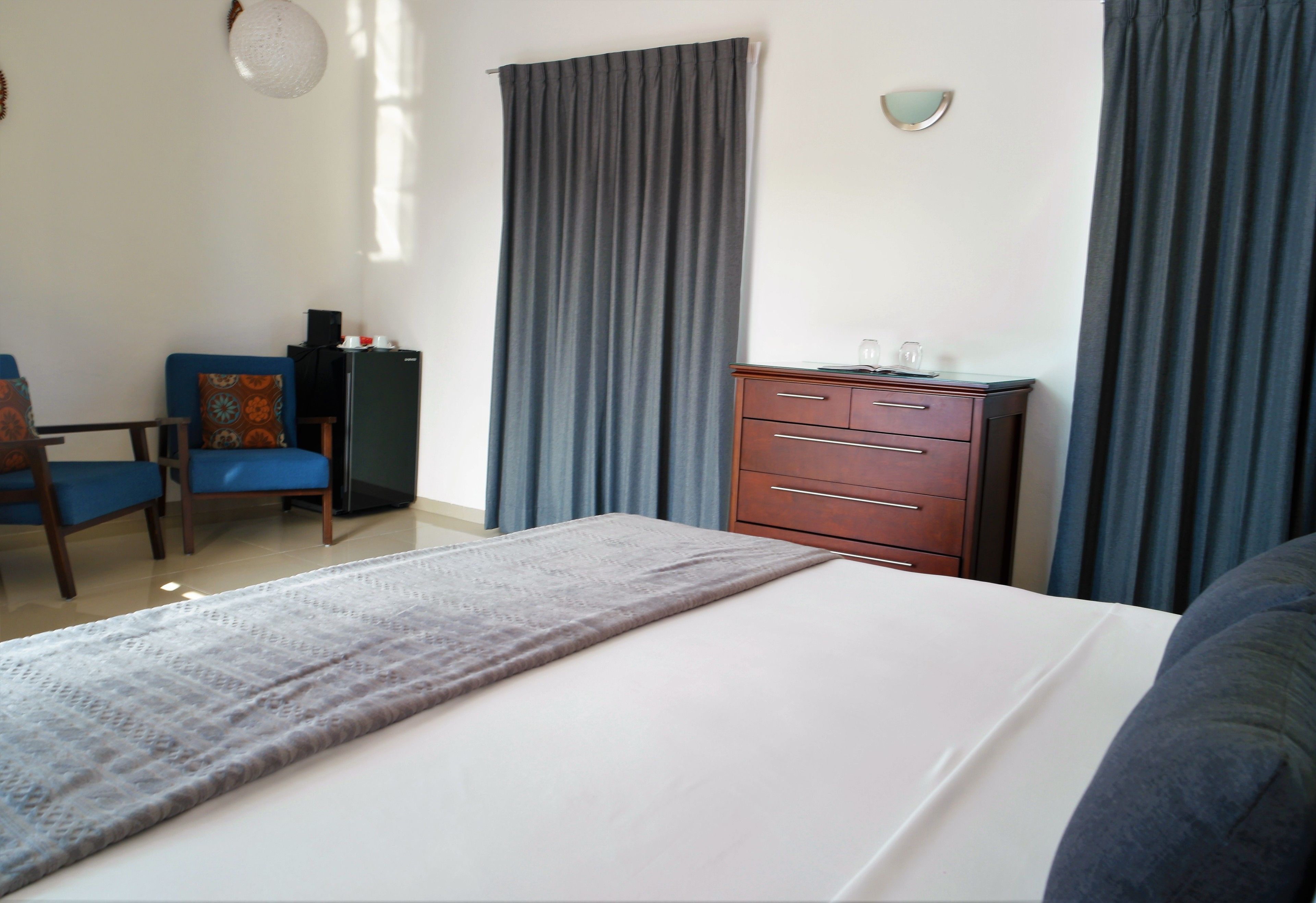 Une chambre d’hôtel comprenant un lit, un bureau avec une chaise, une commode et un luminaire fixé au mur.