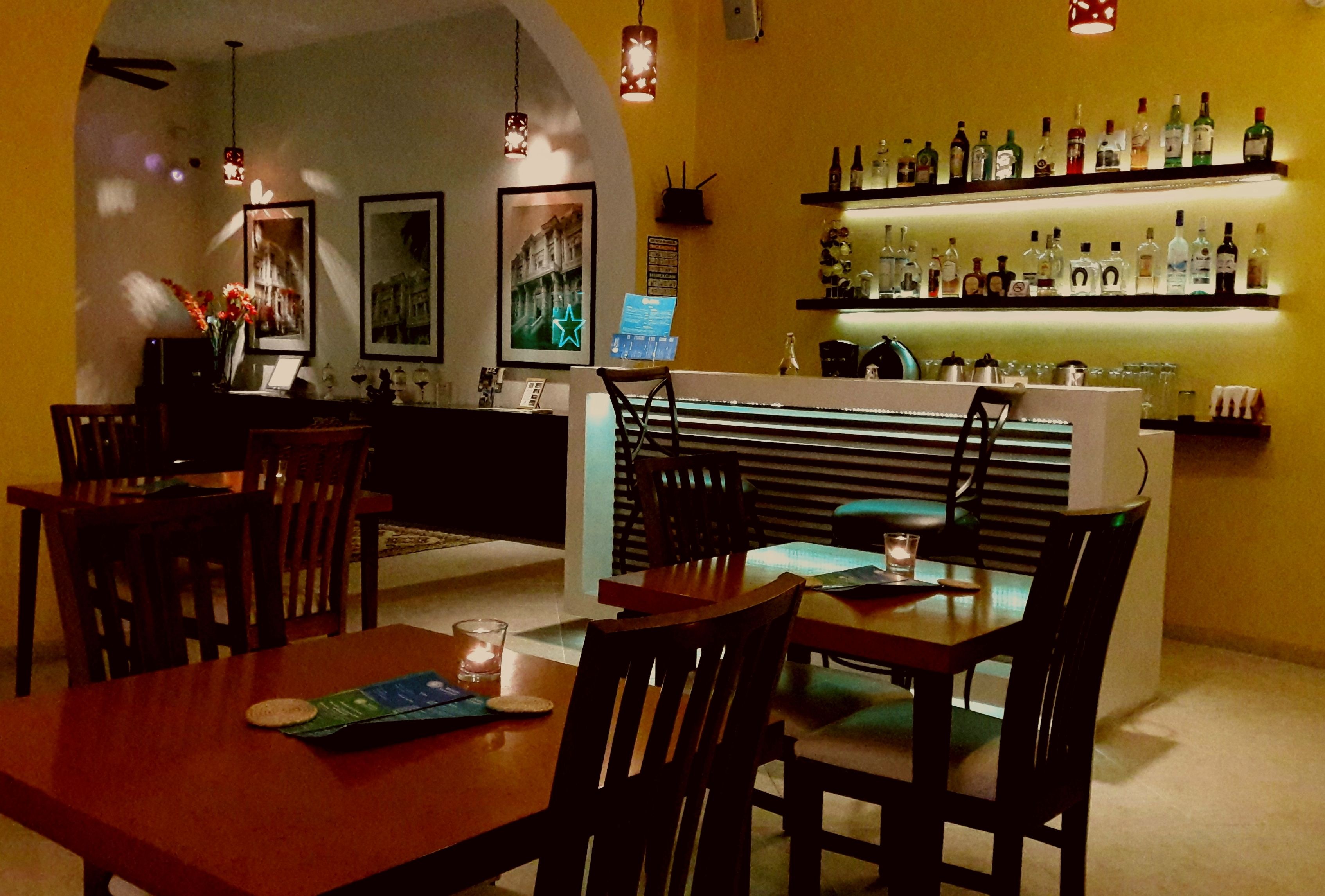 A dimly lit bar area with wooden furniture, a counter with a menu, and shelves stocked with bottles.