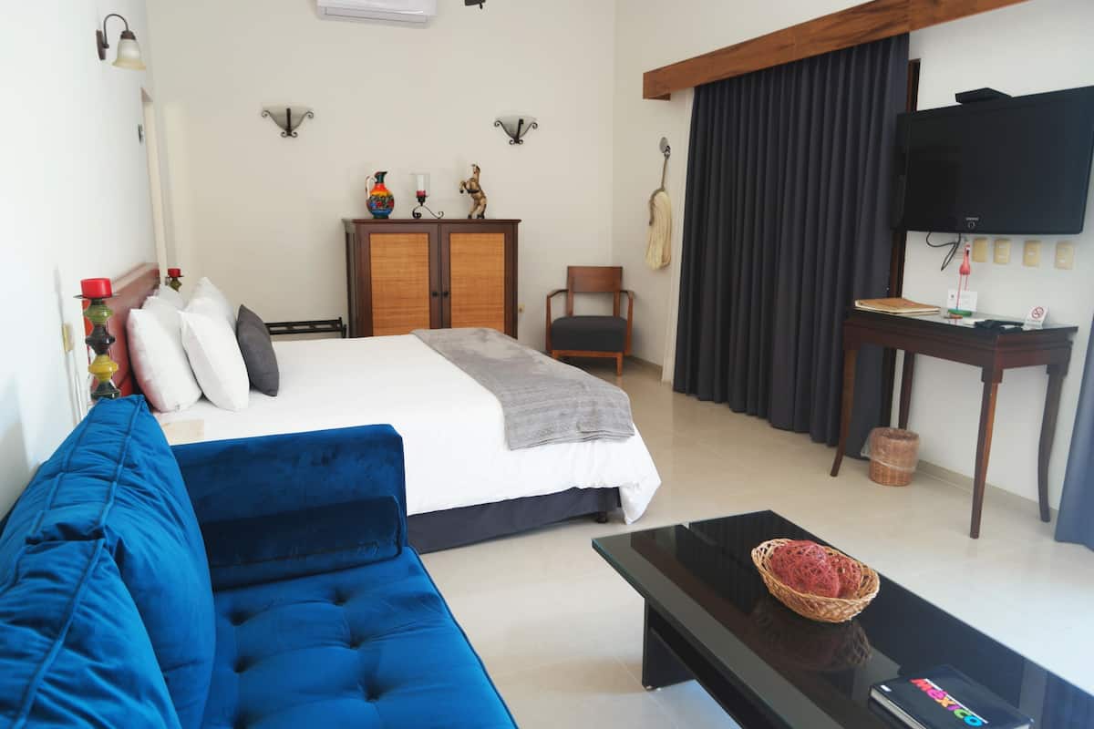 A hotel room with a bed, a blue sofa, a television, and a desk with a basket.