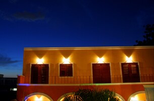 Un edificio con cuatro ventanas iluminadas y fachada roja al anochecer.