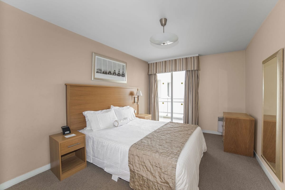 A hotel room with a bed, bedside table, lamp, and a framed picture on the wall.
