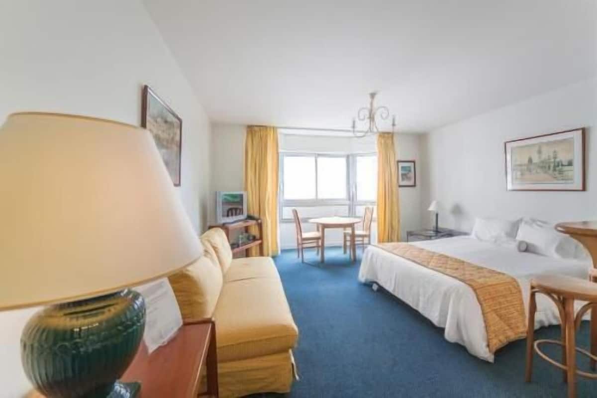 A hotel room with a bed, a sofa, a small table, a chair, a lamp, and a TV.
