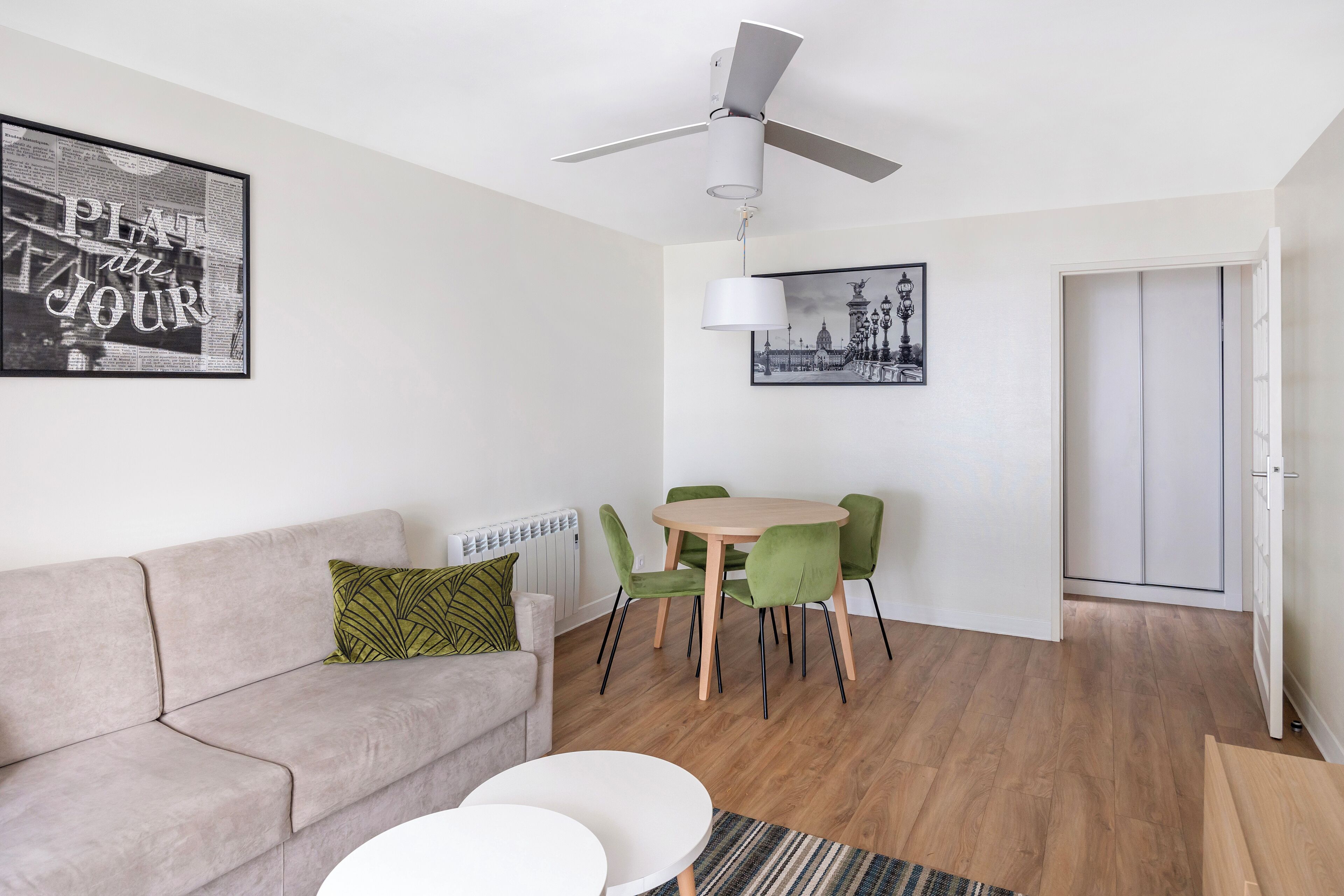 Una sala de estar moderna con un sofá, una mesa de comedor con sillas, un ventilador de techo y dos lámparas de pared.