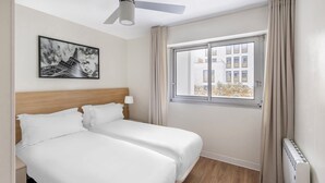 A hotel room with a bed, a ceiling fan, a window with curtains, and a wall-mounted picture of the Eiffel Tower. - Royal Regency Paris Vincennes (Vincennes)