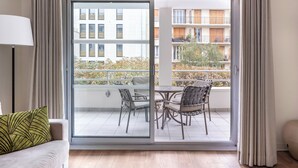 A modern living room with a sofa, a table with chairs, and a sliding glass door leading to a balcony with outdoor furniture. - Royal Regency Paris Vincennes (Vincennes)