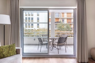 Una sala de estar moderna con un sofá, una mesa con sillas y un ventanal corredizo que da a un balcón con mobiliario exterior.