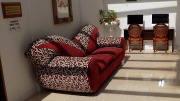 Ein Wohnzimmer mit einem gemusterten Sofa, einem Couchtisch mit geometrischem Design, einem Kamin und einem Essbereich mit zwei Stühlen.