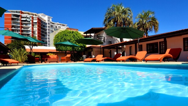 A swimming pool with sun loungers and umbrellas, surrounded by palm trees and a multi-story building. - Hotel Concorde (Punta del Este)