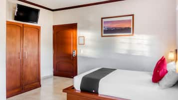 Una camera d'albergo con un letto, una TV fissata al muro, una porta e un quadro incorniciato.