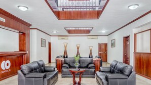 Un vestíbulo con sofás de cuero, una recepción de madera y un jarrón decorativo en el centro.