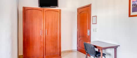Una stanza con un armadio in legno, una televisione montata sopra, una scrivania con una sedia e un quadro appeso al muro.