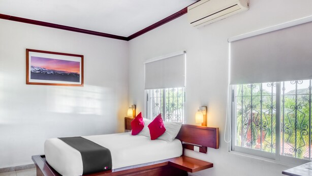 Una habitación de hotel con cama, mesitas de noche, ventana con vistas y aire acondicionado.