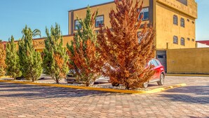 Un edificio con techo plano, varias ventanas y un estacionamiento pavimentado con árboles y un coche rojo.