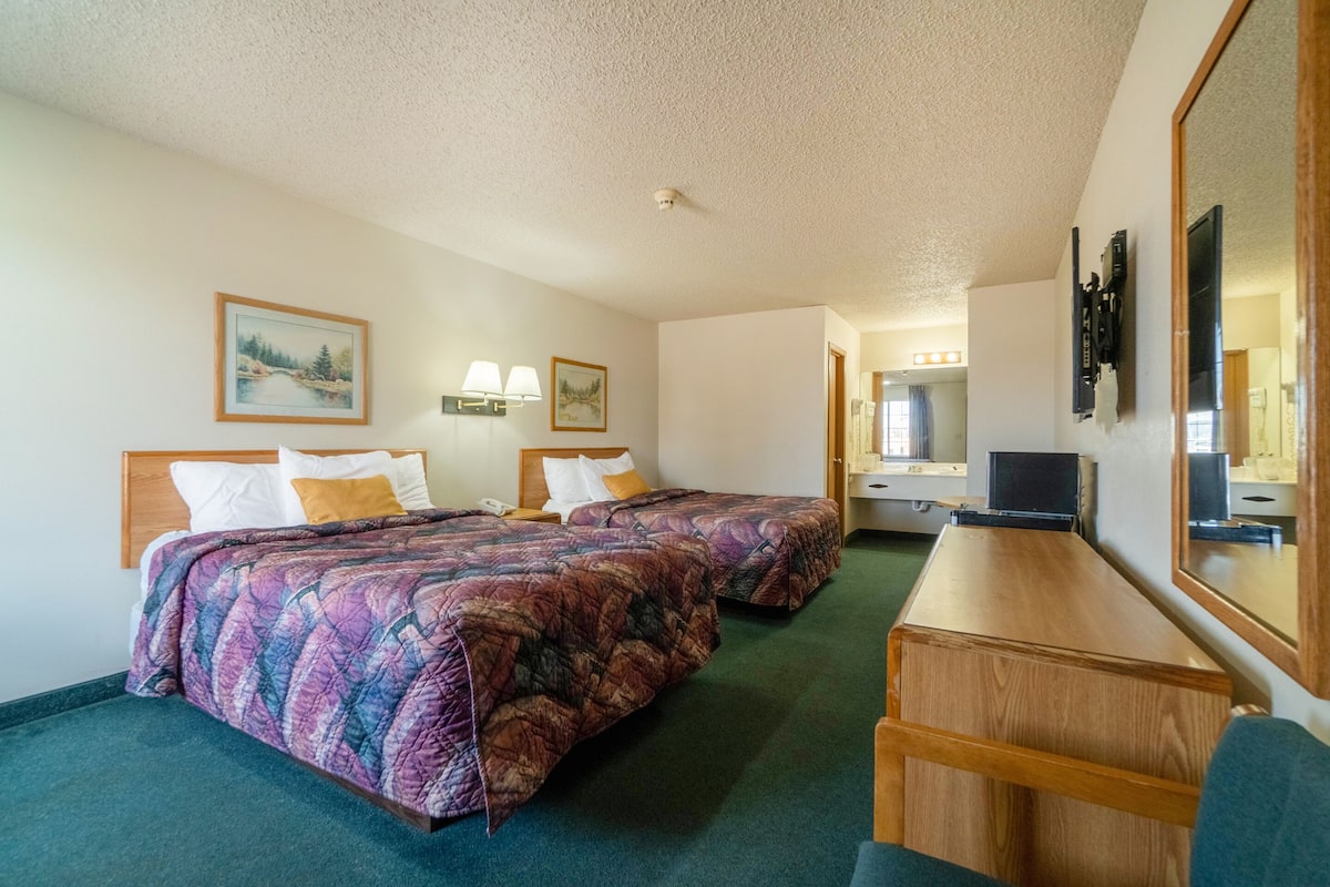 A hotel room with two beds, a desk, a mirror, and a television.