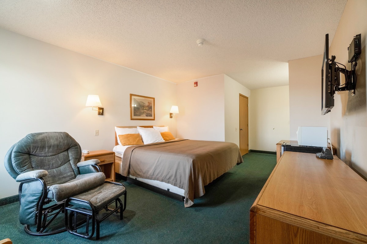 A hotel room with a bed, a reclining chair, a desk, and a flat-screen TV.