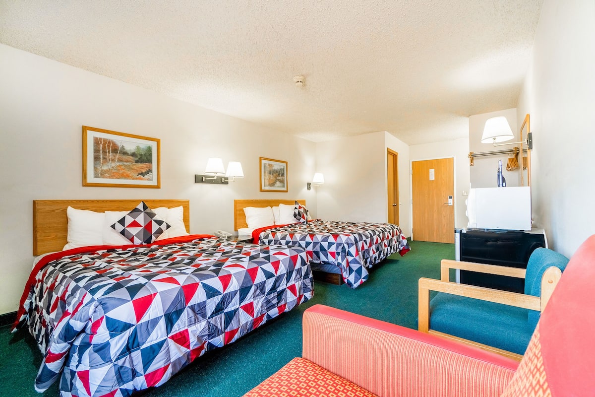 A hotel room with two beds, a chair, a desk, and a mirror.