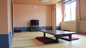 Une pièce avec un sol recouvert de tatamis, équipée d’une télévision, d’une table et d’un futon.