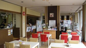 Un restaurant avec des tables et des chaises, un comptoir où figure le menu, et un réfrigérateur.