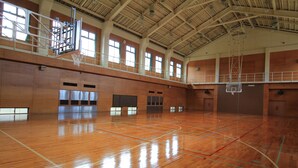 Un terrain de basket-ball intérieur doté d’un plancher en bois, de plusieurs paniers de basket et de grandes fenêtres laissant entrer la lumière naturelle.