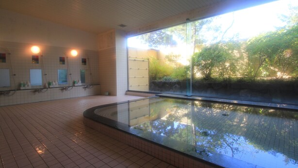 Un espace spa doté d’un grand jacuzzi à débordement, entouré de baies vitrées, d’un sol carrelé et offrant une vue sur la verdure environnante.