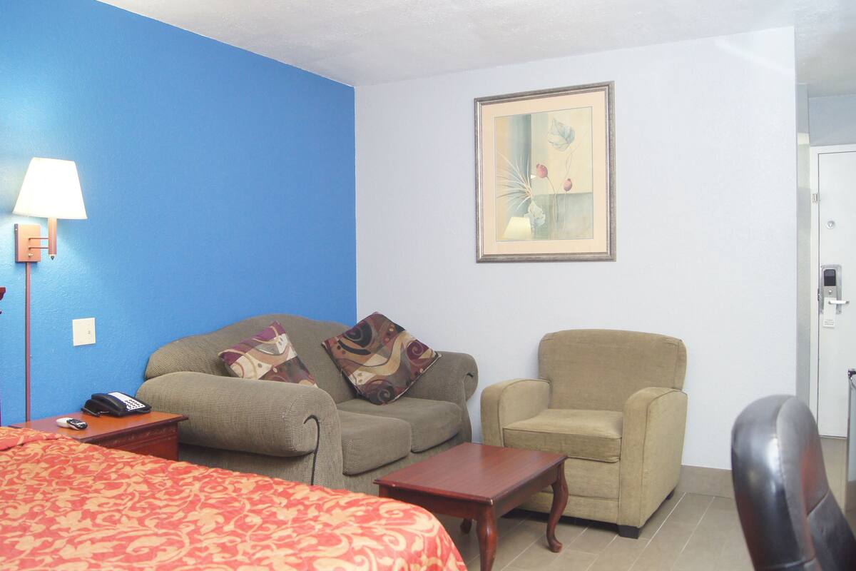 Une chambre d’hôtel avec un lit, un canapé, une chaise, une petite table, une lampe et un tableau au mur.
