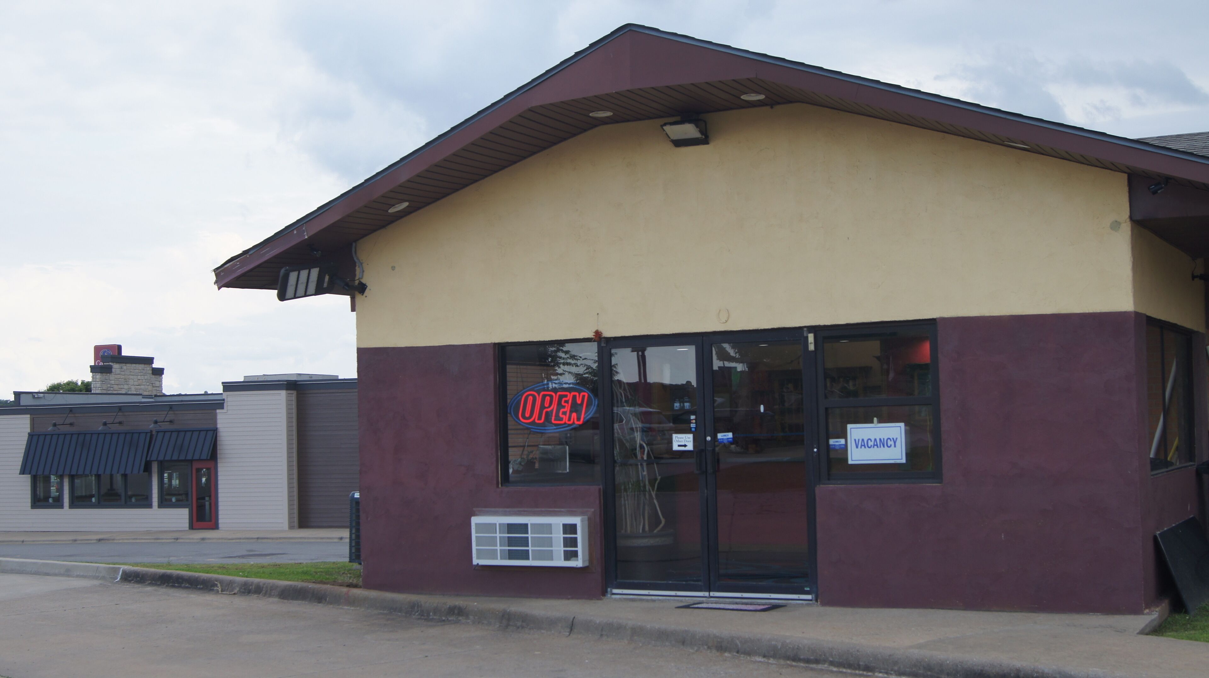 A building with a 'VACANCY' sign, a 'OPEN' sign, and a window with a view of the interior.