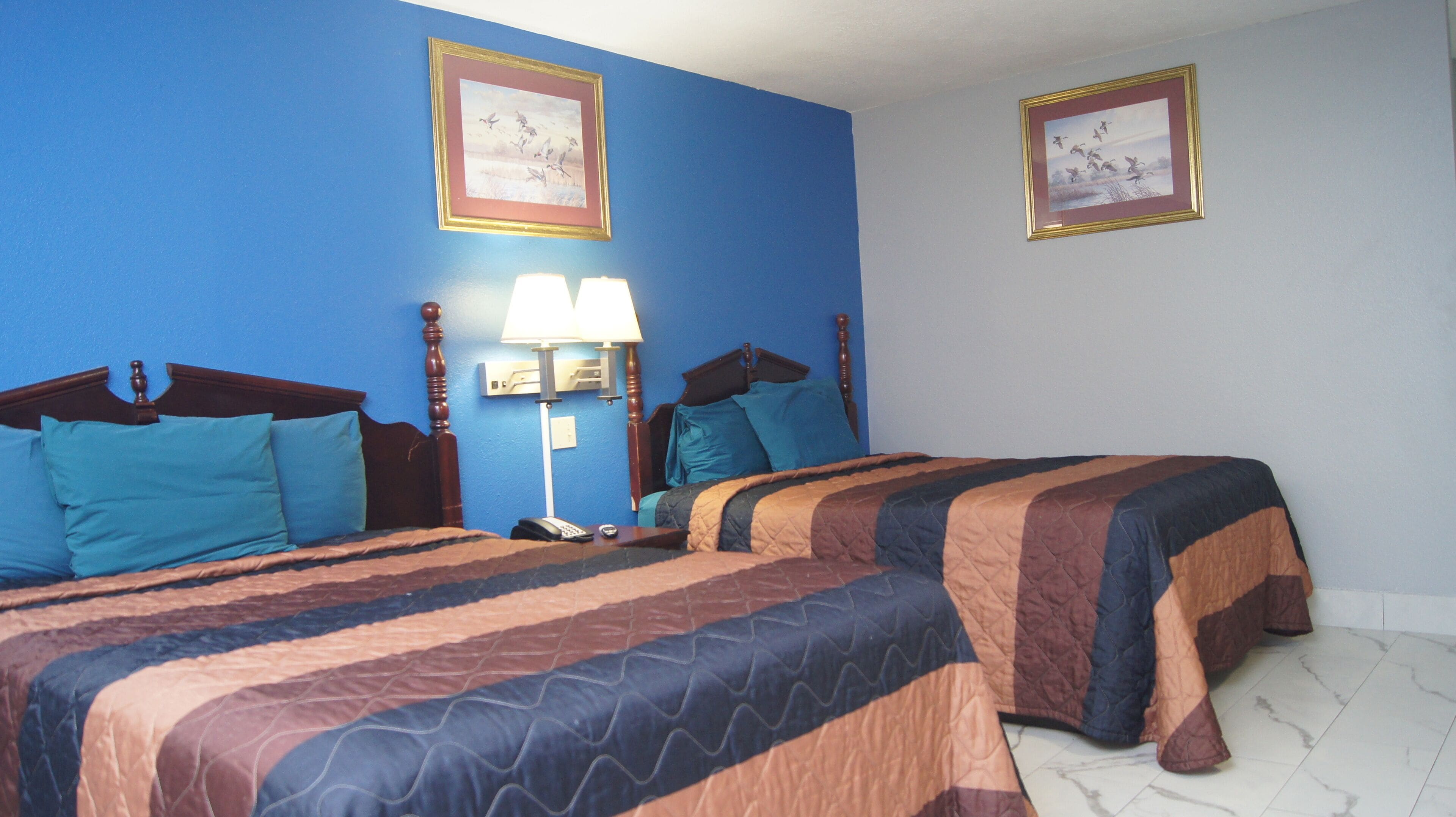 A hotel room with two beds, a nightstand, a lamp, and two framed pictures on the walls.