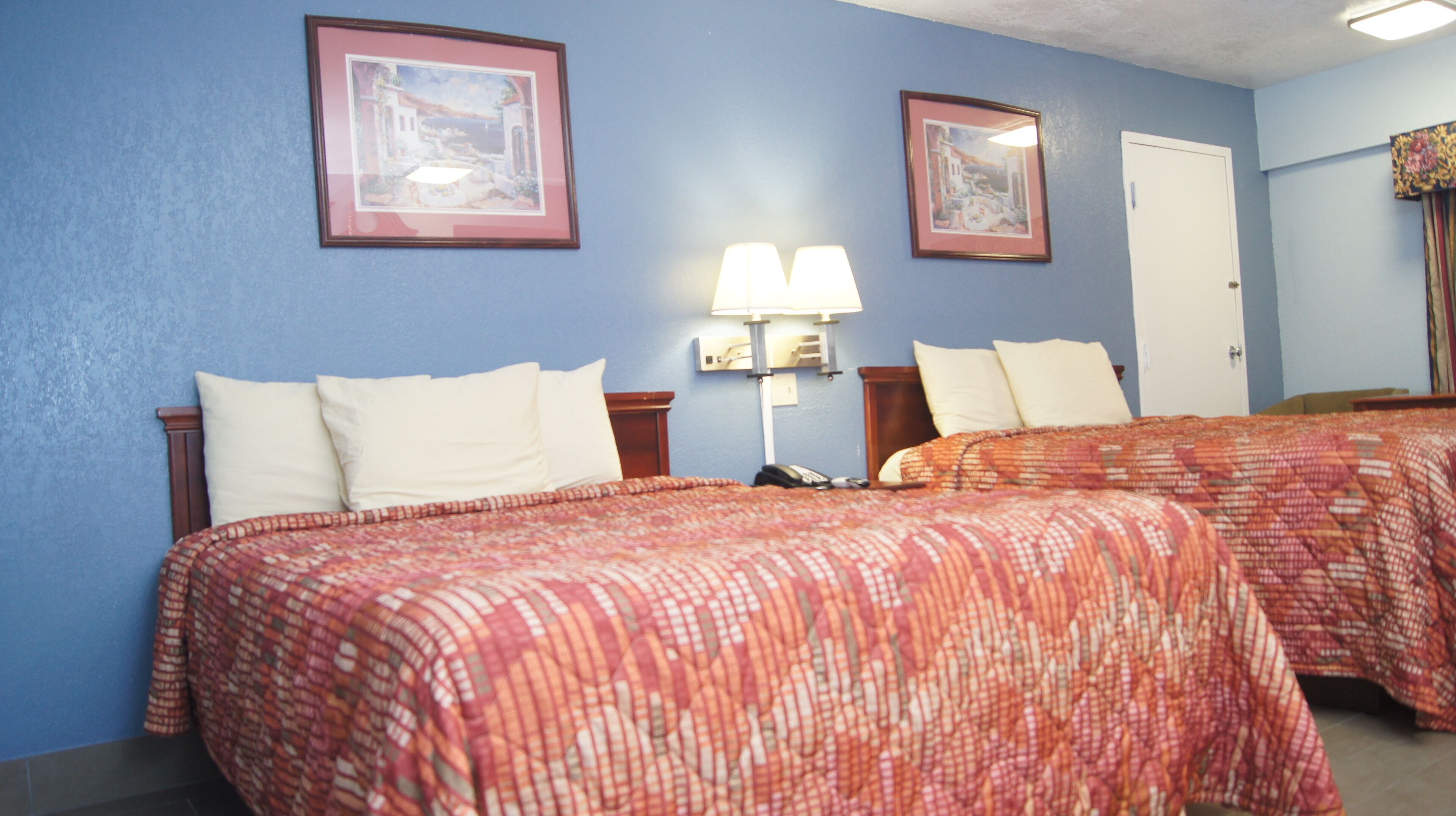 A hotel room with two beds, a nightstand, a lamp, and two framed pictures on the wall.