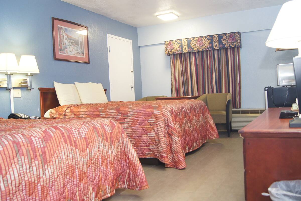 Une chambre d’hôtel avec deux lits, un bureau, une chaise, une télévision et une lampe.